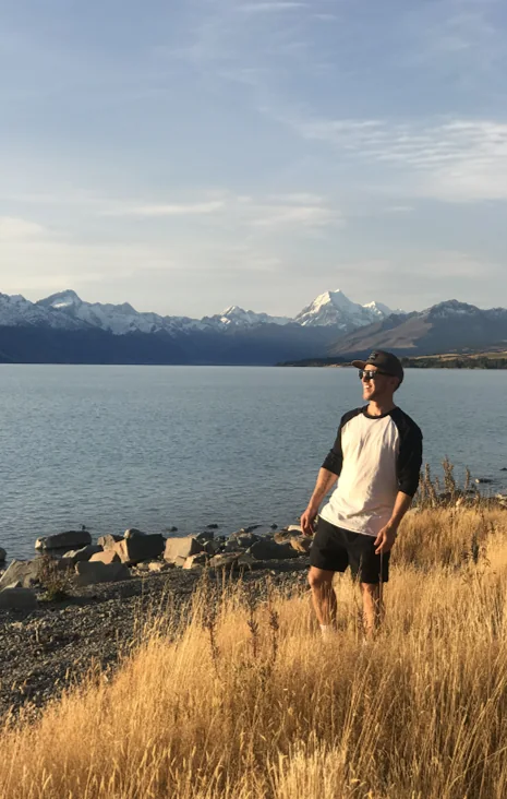 Standing by a lake below snow-capped mountains